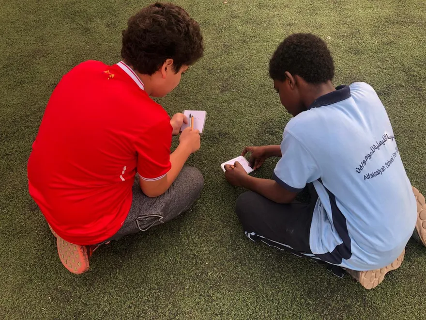 Two students writing notes during a learning activity on the field